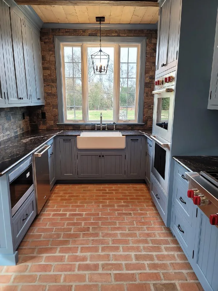 A kitchen with blue cabinets and a brick floor.